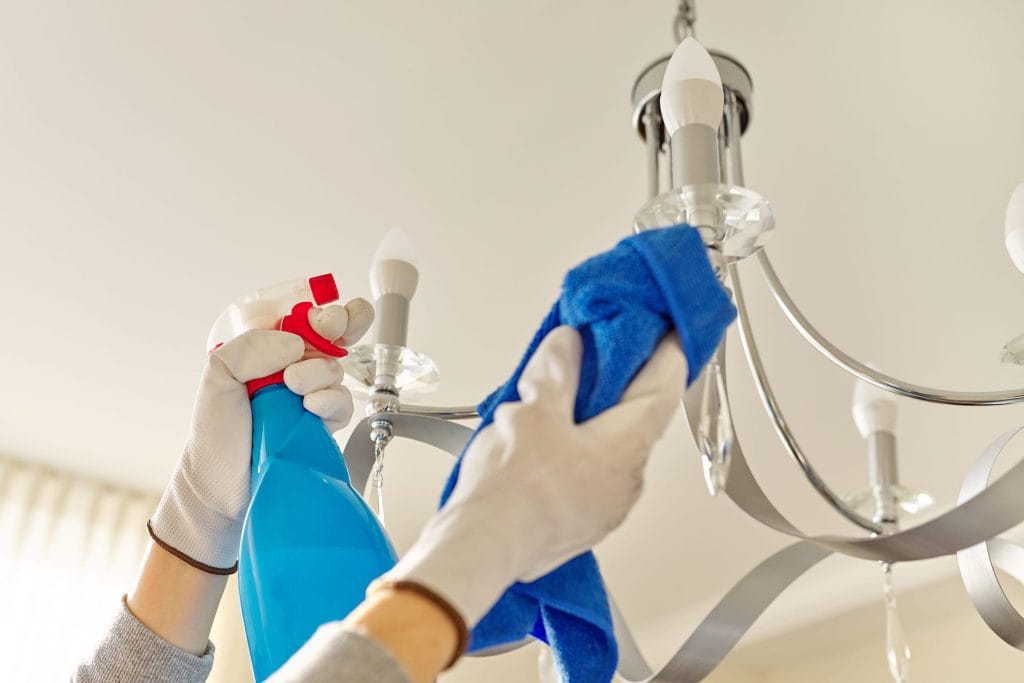 End of lease cleaning Perth: Hands cleaning chandelier with spray and cloth for bond cleaning service.